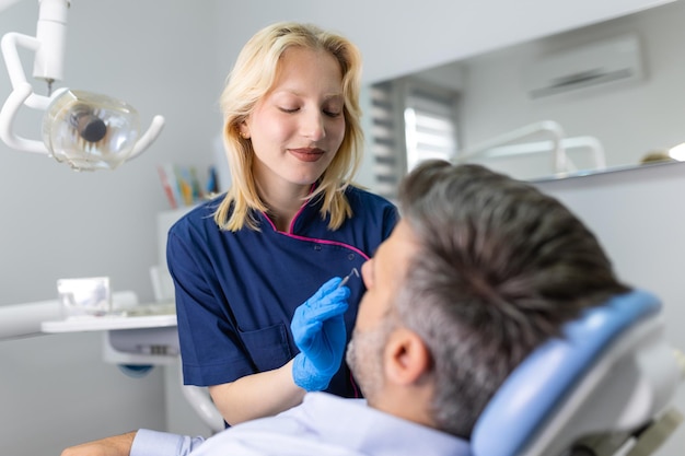 Dentysta w niebieskim mundurze wykonujący zabieg zębów u pacjenta płci męskiej podczas zabiegu we współczesnej klinice dentystycznej