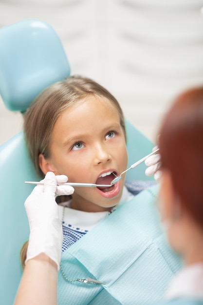 Dentysta w rękawiczkach. Rudowłosa doświadczone dziecko dentysta w białych rękawiczkach bada dziewczynę
