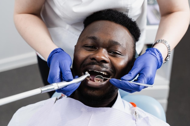 Dentysta wierci zęby i usuwa próchnicę afrykańskiego mężczyzny w klinice stomatologicznej Leczenie zębów Wypełnienie dentystyczne dla pacjenta afroamerykanina