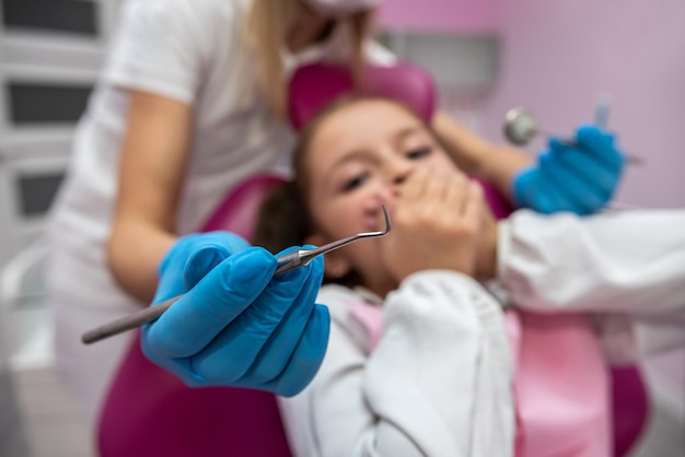 Dentysta wykona zabieg wypełnienia zęba u przestraszonego dziecka w klinice dentystycznej Lekarz używający narzędzi dentystycznych w pracy słodkie dziecko pacjent boi się bólu zęba