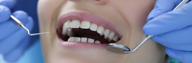 Dentysta z narzędziami stalowymi w rękach bada zbliżenie zębów pacjenta