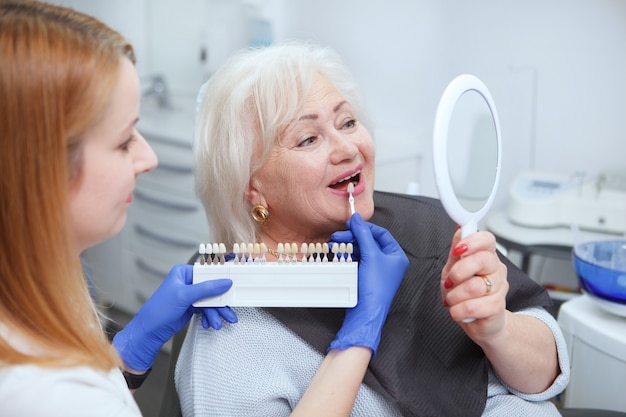 Zdjęcie dentystka pomaga starszemu pacjentowi w wyborze odcienia wybielającego zęby teeth