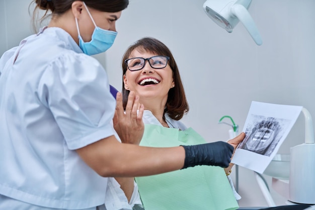 Dentystka rozmawiająca z pacjentką omawiająca zdjęcia rentgenowskie zębów i szczęk