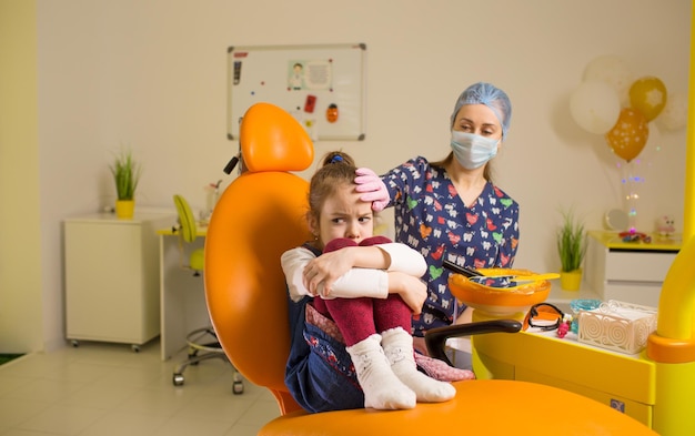 Dentystka uspokaja sfrustrowaną dziewczynkę siedzącą na fotelu dentystycznym podczas wizyty u lekarza