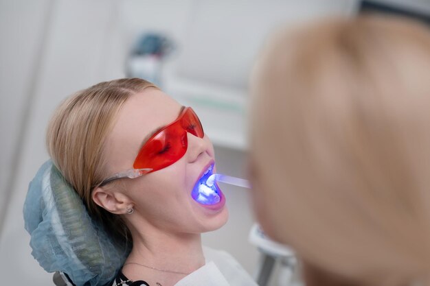 Dentystka Używająca światła Ultrafioletowego Do Wypełnienia Zębów Pacjentki W Okularach Ochronnych