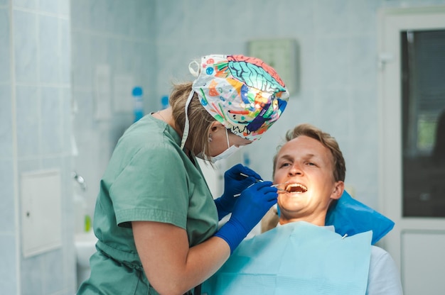 Zdjęcie dentystka w masce w rękawiczkach i czapce z narzędziami w rękach pacjent leży na krześle leczenie