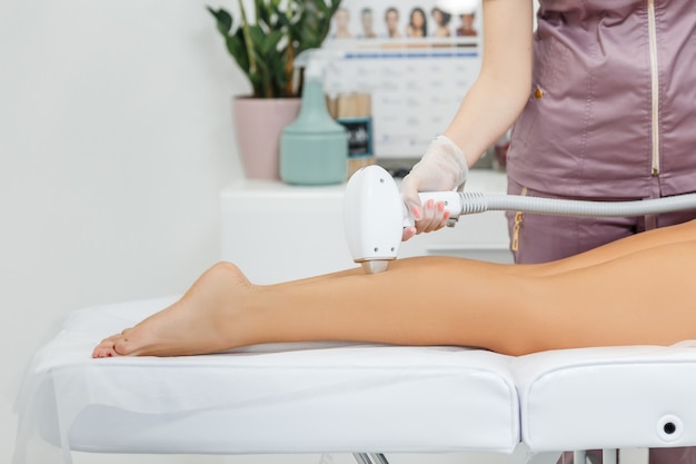 Depilacja laserowa w akcji Kosmetyczka wykonująca depilację laserową na nogach kobiety za pomocą żelu znieczulającego