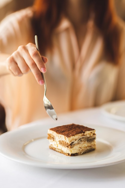 Deser tiramisu. Dziewczyna sięga po deser widelcem. Deserowe zbliżenie