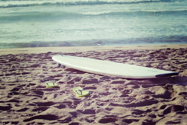 Deska surfingowa i klapki na piasku w stylu vintage