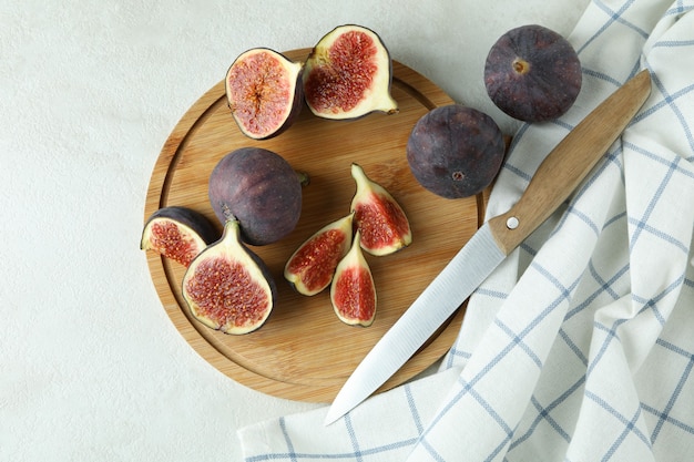 Deska z figą, nożem i ręcznikiem kuchennym na białym teksturowanym stole