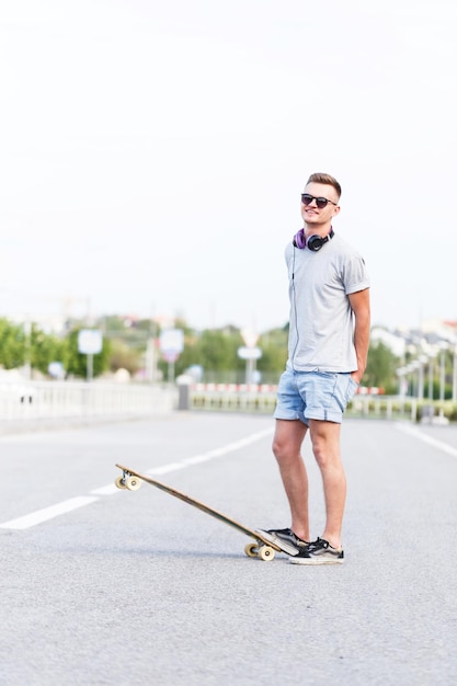 Deskorolkarz ubrany w szarą koszulkę i okulary przeciwsłoneczne zostaje z longboardem na miejskiej drodze