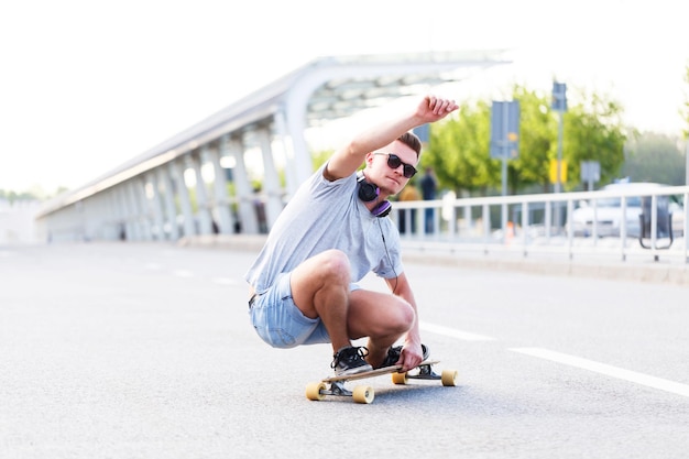 Deskorolkarz w okularach przeciwsłonecznych jeździ na longboardzie po asfalcie w mieście, jazda podstępem w niskiej pozycji