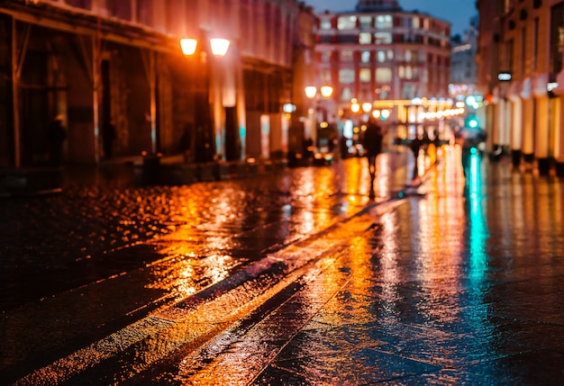 Deszczowa noc w dużym mieście, odbicia światła na mokrej nawierzchni drogi.