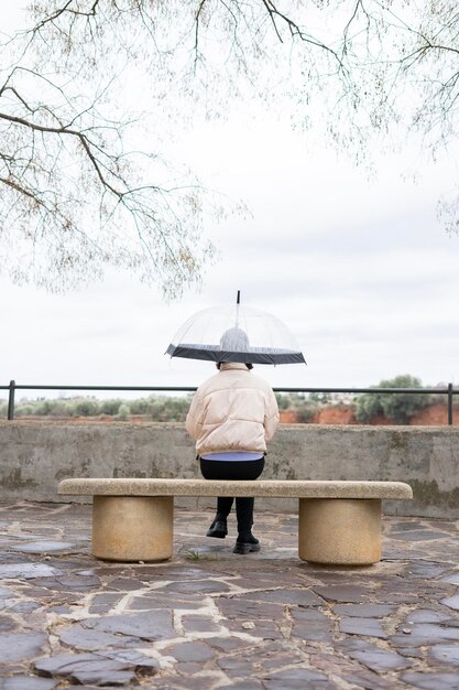 deszczowy dzień Dziewczyna z przezroczystym parasolem siedzi na ławce w deszczu