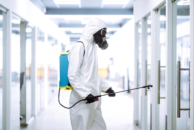 Dezynfekcja biura w celu zapobieżenia COVID19 Mężczyzna w kombinezonie ochronnym z rozpylonymi chemikaliami