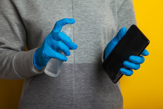 dezynfekcja telefonu. Kobieta w gumowych rękawiczkach trzyma w rękach telefon i spray dezynfekujący.