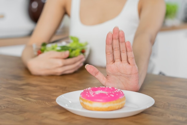 Dieta Dieta azjatycka młoda kobieta lub dziewczyna użyj ręki wypchnij odmowę słodkiego pączka i wybierz pomidorową mieszankę sałat warzywa jedz jedzenie dla dobrego zdrowego zdrowia, gdy jesteś głodny Zbliżenie kobieta odchudzająca się