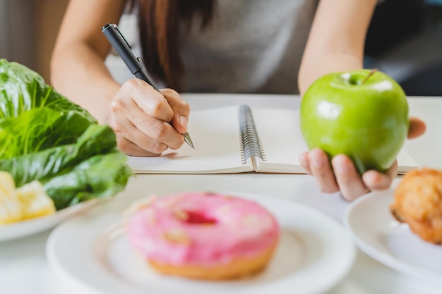 Dieta dieta azjatycka młoda kobieta pracująca napisz plan diety prawo odżywianie trzymaj zielone jabłko warzywa sałatka to jedzenie dla dobrego zdrowia nie wybieraj jedz pączki śmieciowe jedzenie Dietetyk odchudzanie osoba