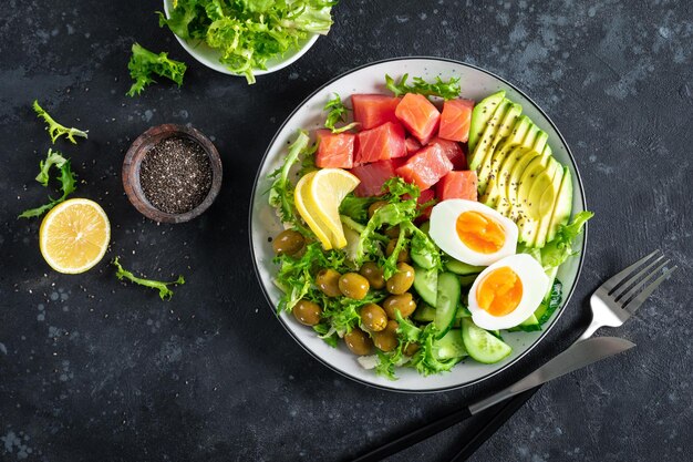 Dieta ketogeniczna miska na lunch z solonym łososiem, cytryną, awokado, oliwkami, gotowanym jajkiem, ogórkiem, zieloną sałatą i nasionami chia, widok z góry trendu zdrowej żywności