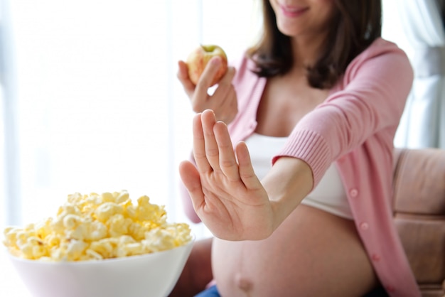 Dieta kobieta w ciąży odmawia popcornu i wybiera czerwone jabłko.