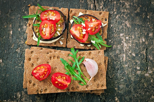 Dieta wegetariańska Kanapki z pieczywem chrupkim z kremowym serem czosnkowym, pieczonym bakłażanem, rukolą i pomidorami koktajlowymi na starym drewnianym