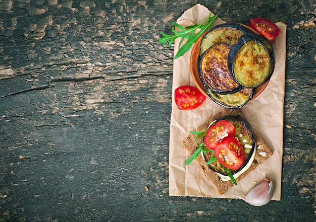 Dieta wegetariańska Kanapki z pieczywem chrupkim z kremowym serem czosnkowym, pieczonym bakłażanem, rukolą i pomidorami koktajlowymi na starym drewnianym