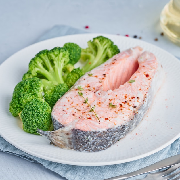 Dieta z łososiem, brokułami, paleo, keto lub papką. Biały talerz na niebieskim stole, widok z boku