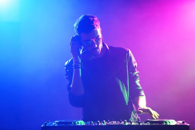 DJ grający muzykę w mikserze na kolorowym mglistym tle