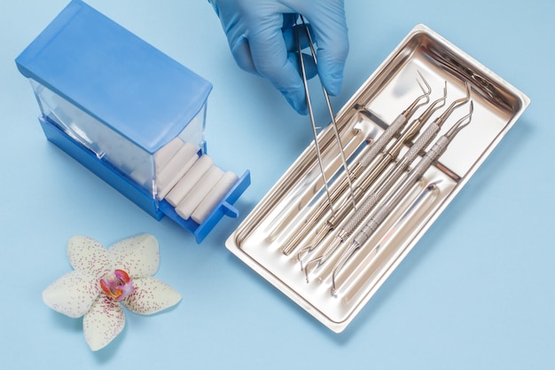 Dłoń dentysty w gumowej rękawiczce z pęsetą i zestawem kompozytowych narzędzi wypełniających do leczenia stomatologicznego w stalowej tacce. Koncepcja narzędzi medycznych. Widok z góry.