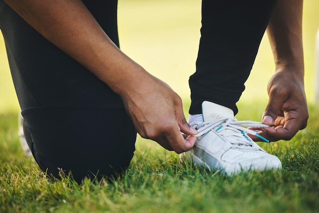 Dłoń i buty osoby do zawodów sportowych na boisku do ćwiczeń lub gry w zbliżeniu Zaangażowanie sportowca lub zawiązanie koronki na torze do wyścigu poprzez zaangażowanie w występ w turnieju lub mecz