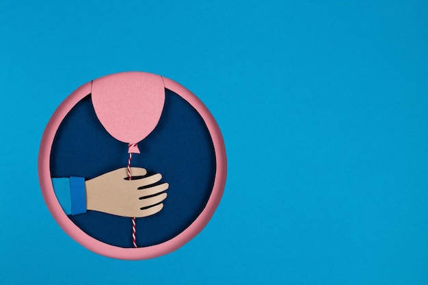 Dłoń trzymająca balony różowy papier w pokrywają niebieski okrągły otwór, różowe koło ramki. Koncepcja wakacje, urodziny, Walentynki. Sztuka papieru 3D i styl origami. Świętuj plakaty z banerami wydarzeń