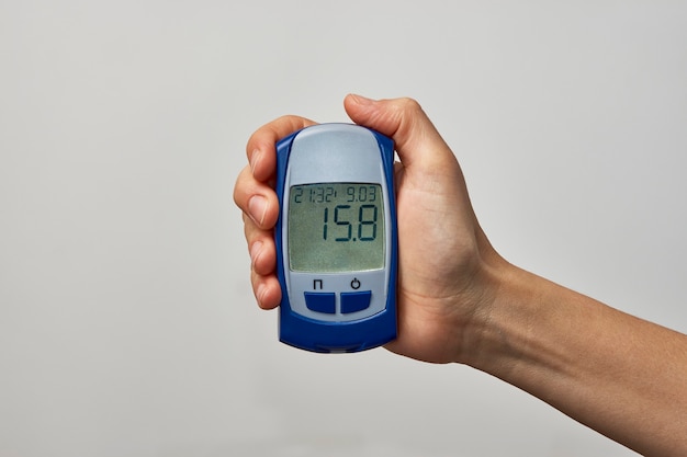 Dłoń trzymająca glukometr z wynikiem badania poziomu cukru we krwi. Womans strony pokazujące test cukru, na białym tle z miejsca na kopię