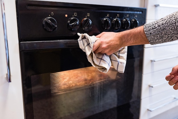 Dłoń trzymająca ściereczkę otwierającą drzwi piekarnika w kuchni