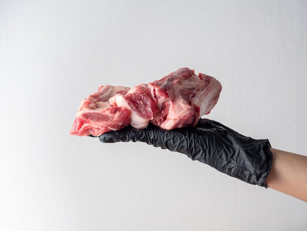 Dłoń w czarnej rękawiczce trzyma kawałek surowego mięsa na jasnym tle.