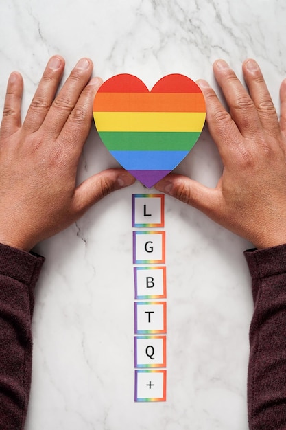 Dłonie dojrzałego mężczyzny umieszczające serce z kolorami ruchu nad akronimem LGBTQ