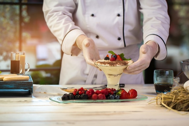 Dłonie dotykają szkła z deserowymi jagodami na kremie świeżo zrobionym słodkim daniem tiramisu z kuchni włoskiej
