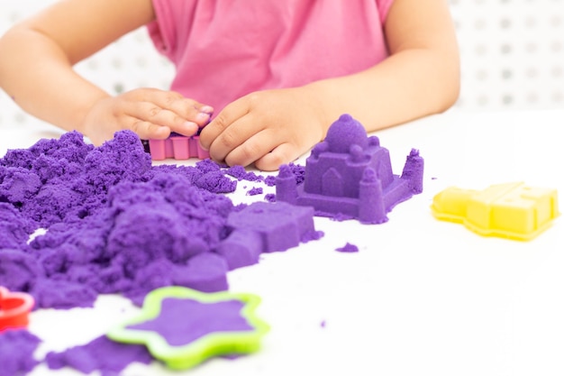 Dłonie dzieci bawią się piaskiem kinetycznym w kwarantannie. fioletowy piasek na białym stole. koronawirus pandemia