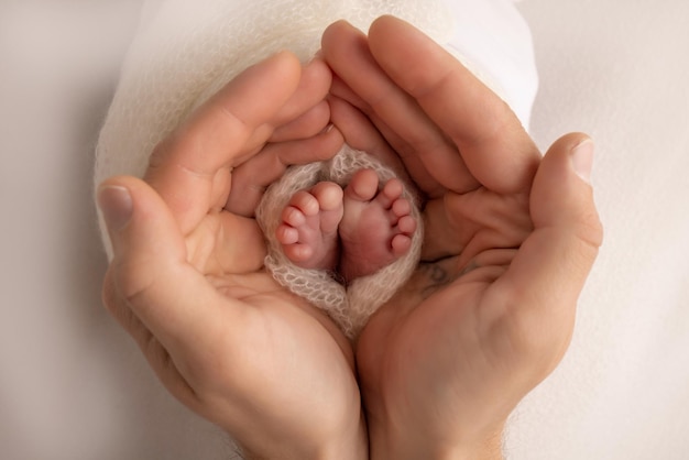 Dłonie rodziców Ojciec i matka trzymają stopy noworodka w białym kocyku na białym tle Stopy noworodka w rękach rodziców Zdjęcie stóp na piętach i palcach
