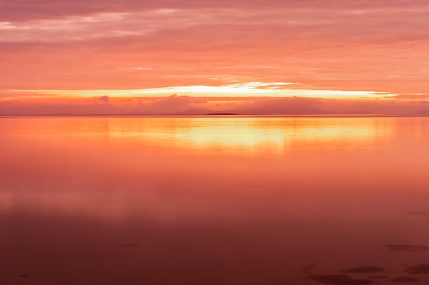 Długa ekspozycja promiennego wschodu słońca z różowożółtymi kolorami odbitymi w gładkiej powierzchni oceanu na wyspie Iriomote plaży Nakano