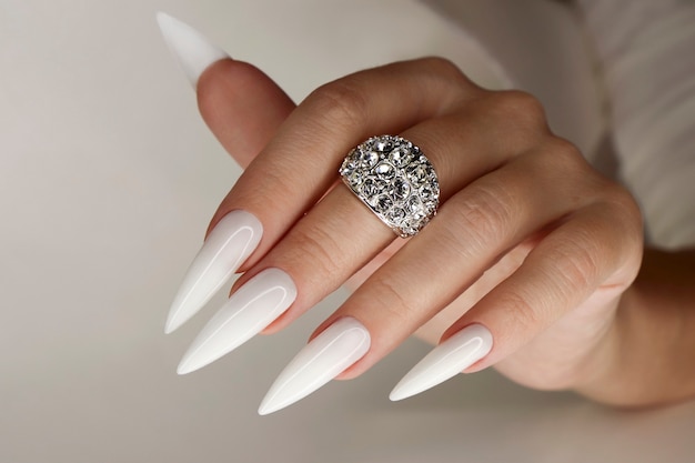 Długi lekki manicure z biżuterią na kobiecej dłoni