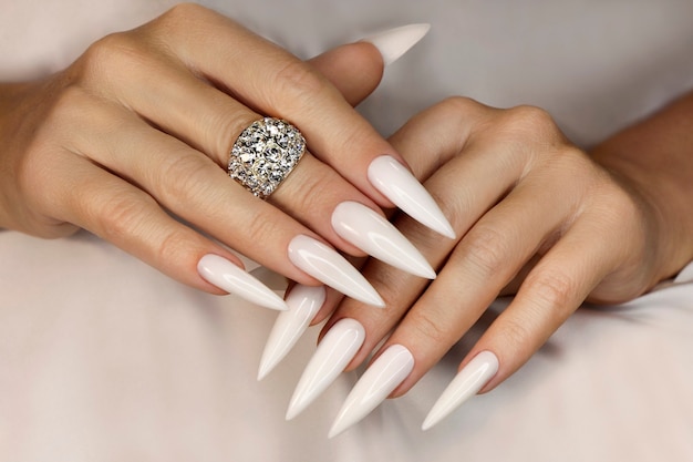 Długi lekki manicure z biżuterią na kobiecej dłoni