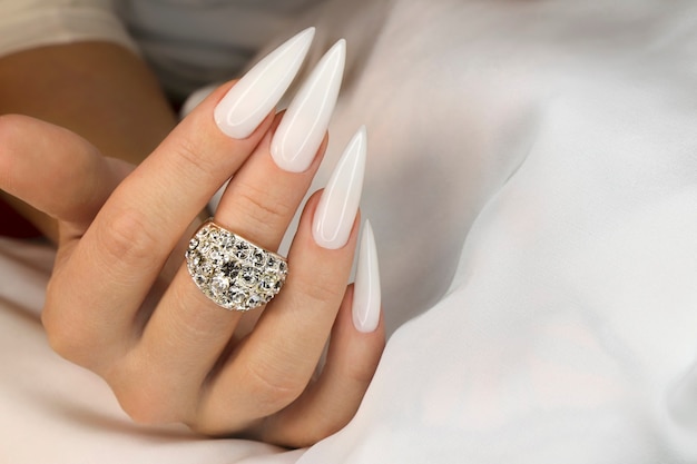 Długi lekki manicure z biżuterią na kobiecej dłoni