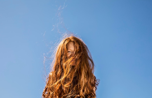 Długie rude włosy zakrywające twarz dziewczyny pod błękitnym niebem