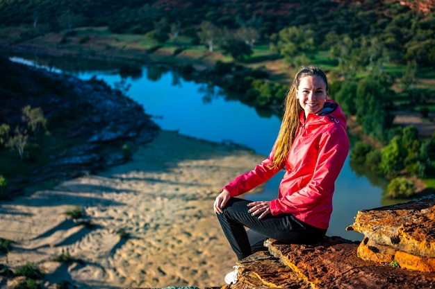 długowłosa dziewczyna siedzi na szczycie wzgórza na czerwonych skałach parku narodowego kalbarri w zachodniej australii