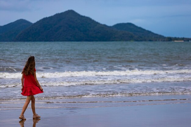 długowłosa dziewczyna w czerwonej sukience spaceruje po tropikalnej australijskiej plaży z wyspami w tle
