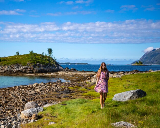 długowłosa dziewczyna w kolorowej sukience spaceruje nad morzem na wyspie senja w norwegii