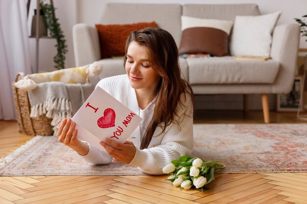 Do 8 marca kobieta trzyma pocztówkę i leży na podłodze w salonie obok bukietu tulipanów