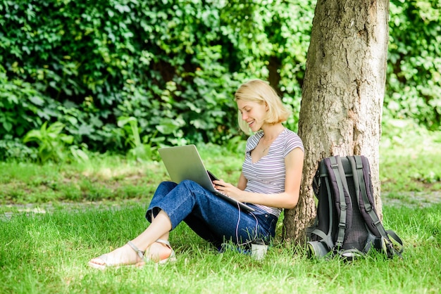 Dobre samopoczucie i zdolność natury są produktywne. Dziewczyna pracuje z laptopem w parku. Powody, dla których powinieneś zabrać swoją pracę na zewnątrz. Student kobieta siedzi na trawie podczas nauki. Praca w letnim parku.