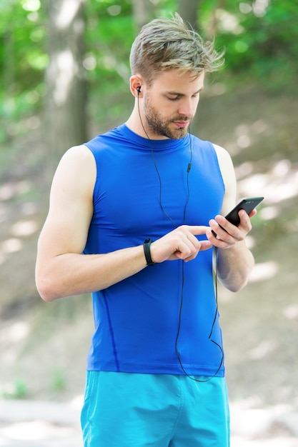 Dobre wyniki muskularny mężczyzna w fitness bransoletka użyj aplikacji sportowej na telefonie cyfrowy sport inteligentny zegarek dla fitness wysportowany mężczyzna w odzieży sportowej trening na świeżym powietrzu Aplikacja fitness Ui ux concept gadżet sportowy