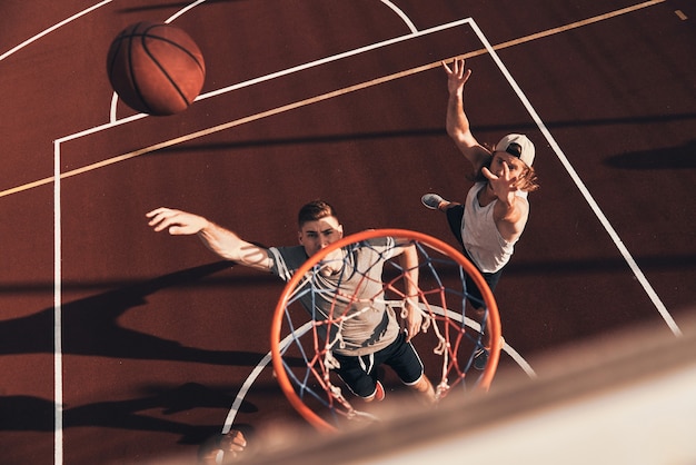 Zdjęcie dobry strzał! widok z góry na młodego mężczyznę w odzieży sportowej, który wykonuje wsad podczas gry w koszykówkę na świeżym powietrzu